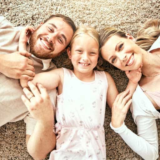 Long distance movers page image of a girl with her parents all smiling lating on a carpeted floor